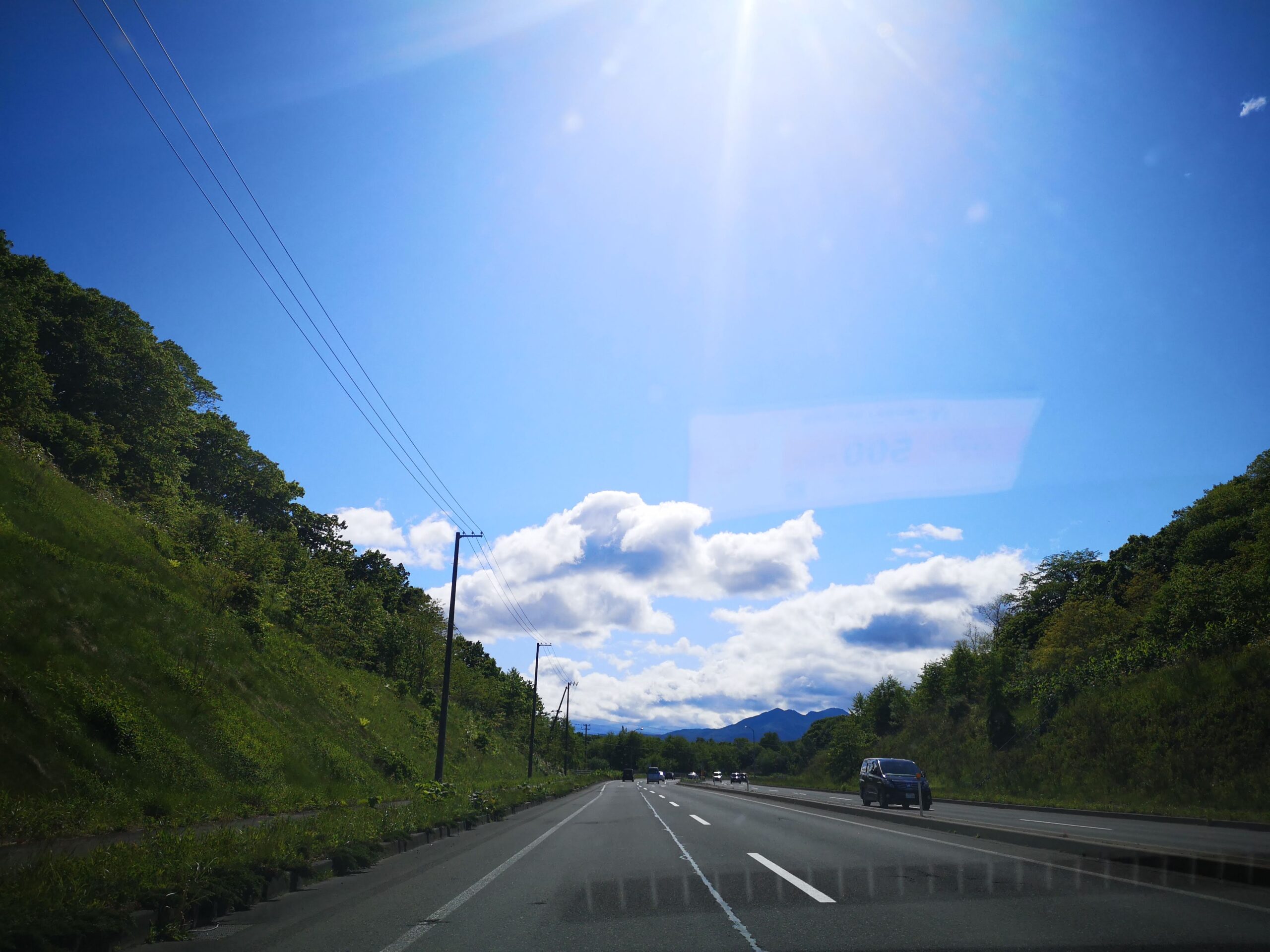 車内から見た北海道の高速道路。青空と緑の山が続く