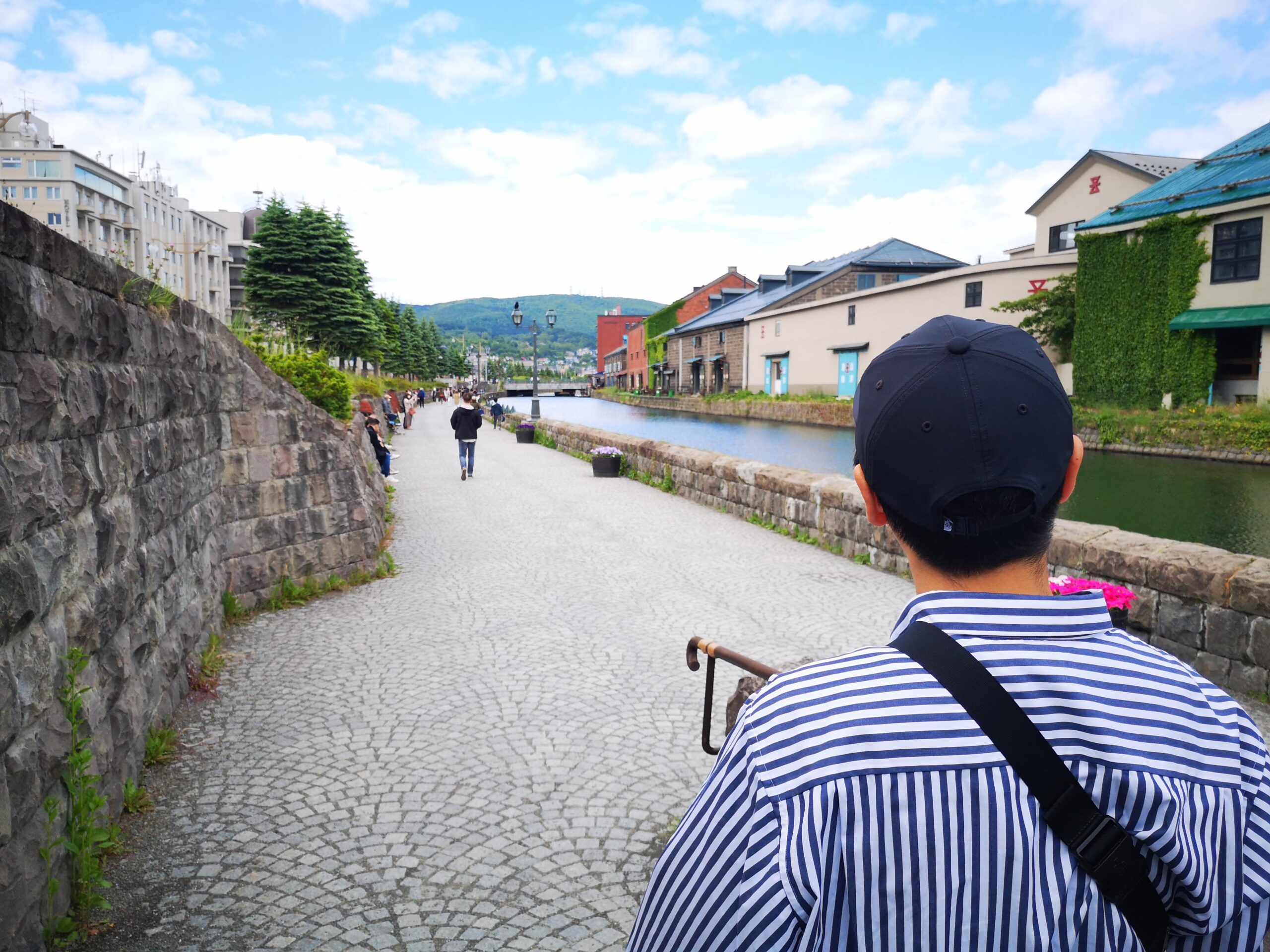 小樽運河沿いを歩く旅行者の後ろ姿。石畳の遊歩道と倉庫群